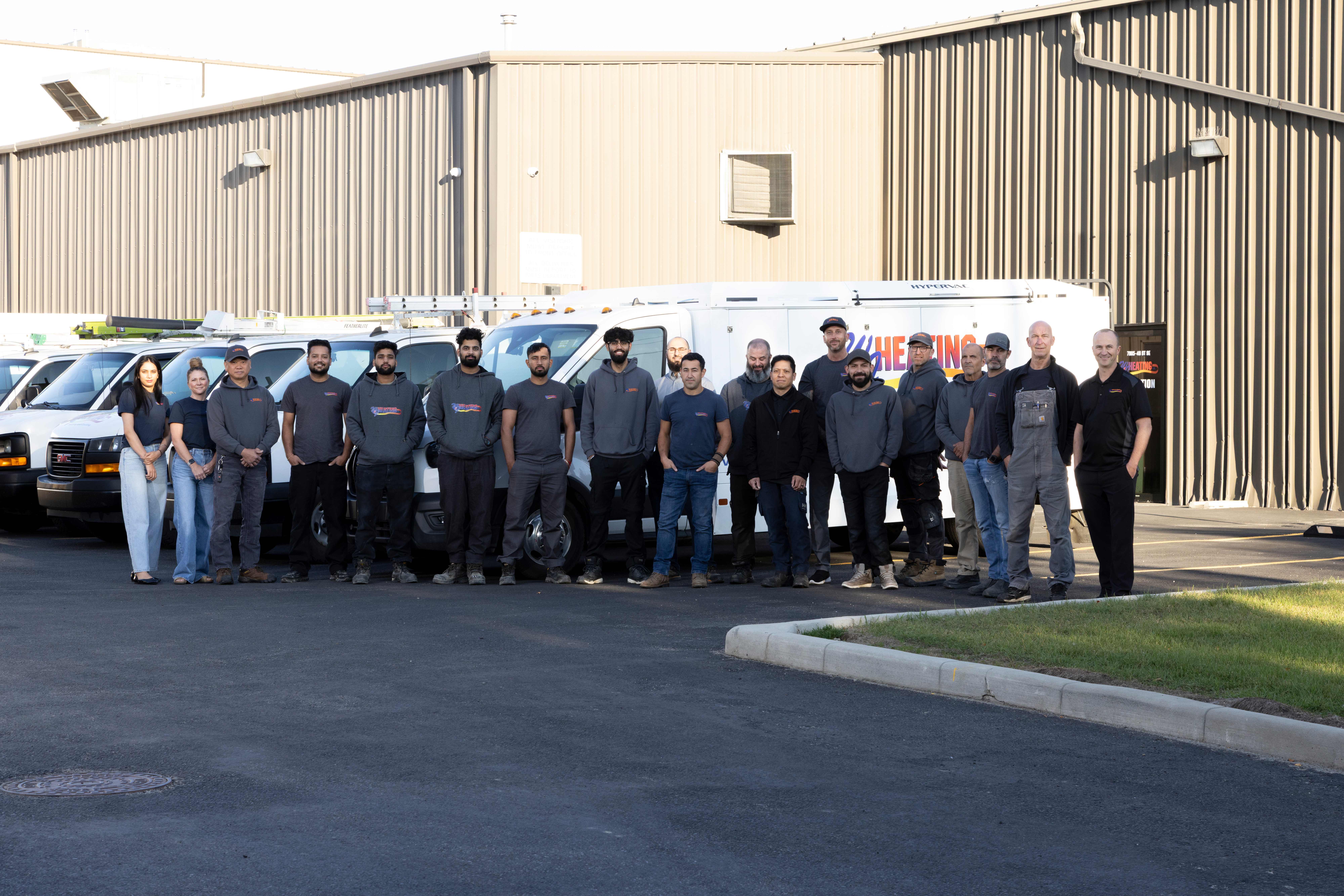 The W & J Heating team standing together in front of their white service vans outside the Calgary facility