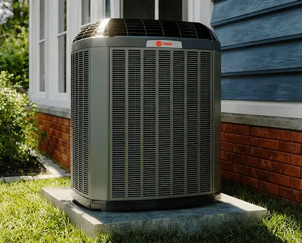 A Trane outdoor air conditioning unit on a concrete pad beside a home with red brick and blue siding